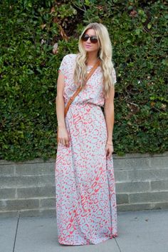 a woman standing on the sidewalk wearing a long dress with an orange and blue print