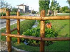 a wooden fence in front of a lush green field and road with houses on the other side