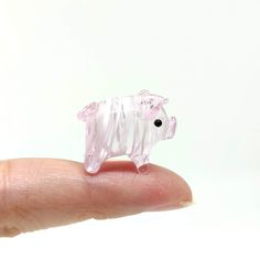 a small glass pig sitting on top of a persons finger in front of a white background