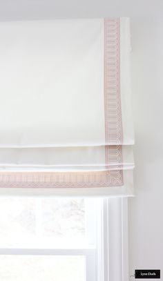 a window with a white and pink roman blind on it's side, in front of a window sill