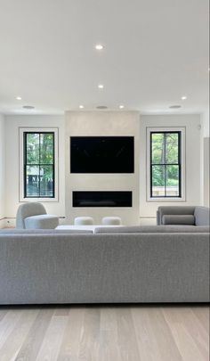 a modern living room with white walls and wood flooring, two large windows on the far wall