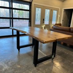 a wooden table sitting inside of a living room next to a brown leather couch and sliding glass doors