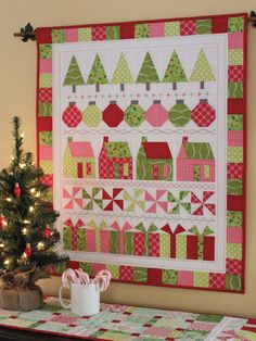 a christmas quilt hanging on the wall next to a table with a small tree in front of it