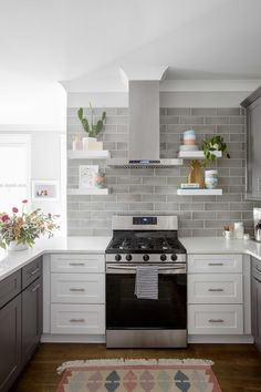 a kitchen with white cabinets and gray tile backsplash, stainless steel range hood