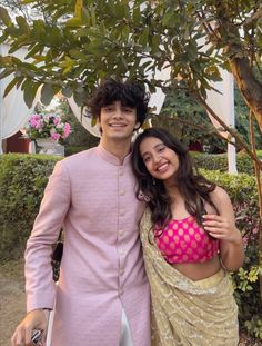 a young man and woman posing for a picture in front of a tree with flowers