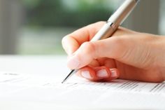 a woman's hand holding a pen and writing on paper