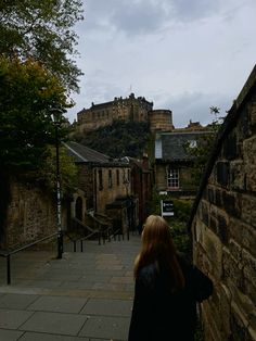 a woman standing on the side of a road next to a stone wall and castle