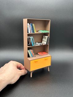 a hand reaching for a book shelf with books on it and a yellow drawer underneath