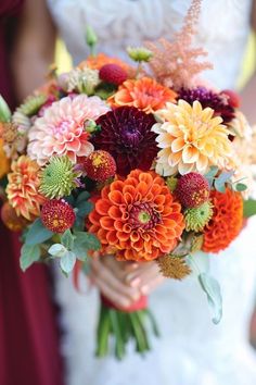 a bride holding a bouquet of orange and red flowers with greenery in her hands