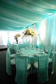 a table set up with white chairs and green drapes