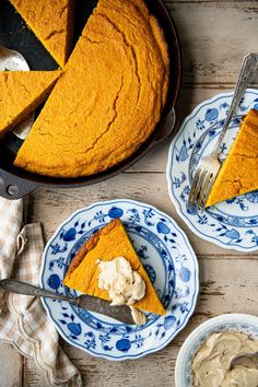 two plates with slices of pumpkin pie on them next to a skillet filled with whipped cream