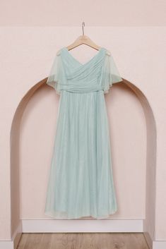 a dress hanging on a hanger in front of a pink wall and wooden floor