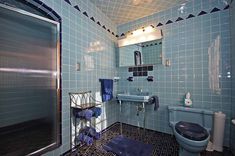 a blue tiled bathroom with a toilet, sink and shower