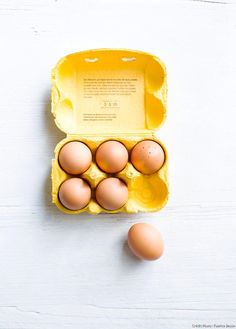 an open carton of eggs sitting on top of a white table next to two brown eggs