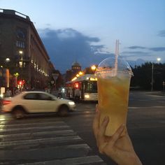 a person holding up a drink in front of a car on the street at night