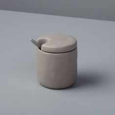 a white container with a spoon sticking out of it's lid on a gray surface