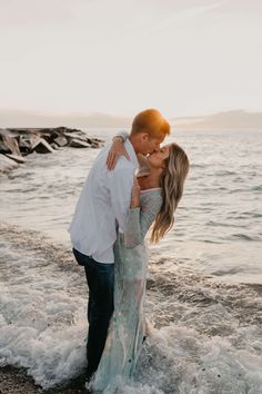 a man and woman kissing on the beach in front of the ocean with waves crashing around them