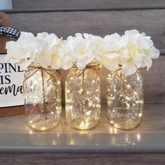 three mason jars filled with white flowers and fairy lights