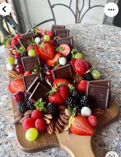 a wooden platter filled with chocolate covered strawberries and other fruit on top of a table