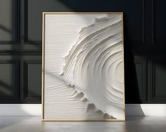 an abstract white painting in a gold frame on the floor next to a black wall