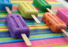 four popsicles with different colored toppings sitting on a colorful table cloth, one is half eaten