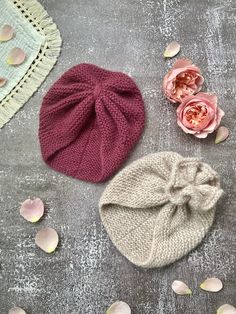 three knitted hats on a table with flowers and petals scattered around the top one has a knot at the bottom