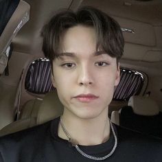 a young man sitting in the back seat of a car wearing a black shirt and silver necklace