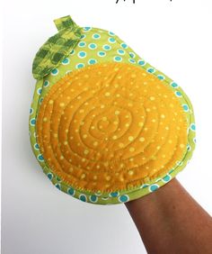 a hand is holding a yellow and green object with polka dots on it, in front of a white background