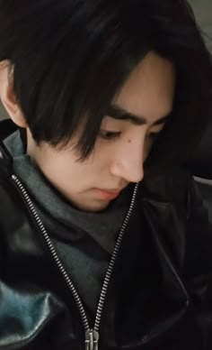 a man with black hair wearing a leather jacket and looking down at his cell phone