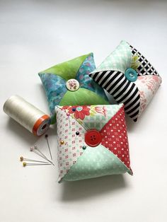 four pillows with different designs and buttons on them sitting next to spools of thread