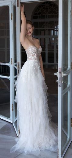 a woman in a white wedding dress is standing outside an open door with her hand up