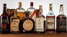 an assortment of liquor bottles sitting on top of a wooden table next to each other