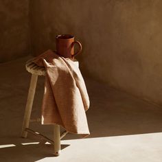 a brown mug sitting on top of a wooden stool next to a tan blanket draped over it