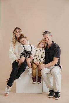 a family posing for a photo in front of a beige background with the child sitting on her dad's lap