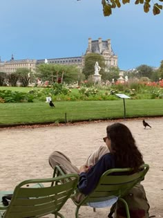 a woman sitting on top of a green lawn chair next to a lush green park