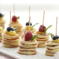 small pancakes with fruit on top and toothpicks sticking out of the stacks are ready to be eaten