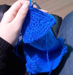 a person is knitting something with blue yarn on their lap and holding it in one hand