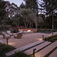 an outdoor fire pit surrounded by seating and trees at night with lights shining on it