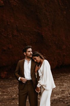 a man and woman standing next to each other in front of a rock formation holding hands