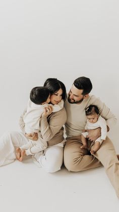 a man and woman sitting on the floor with two babys in their arms, holding each other