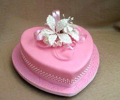 a pink heart shaped cake with white flowers on top