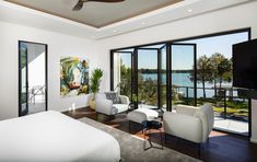 a bedroom with white furniture and large glass doors leading to a balcony overlooking the water