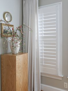 there is a vase with flowers on top of a cabinet next to a window in the room