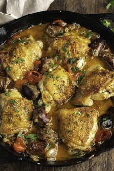 a skillet filled with chicken and vegetables on top of a wooden table