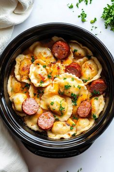 a black bowl filled with pasta and sausage on top of a white tablecloth next to a napkin