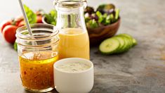 several different types of food in glass jars on a table with vegetables and sauces