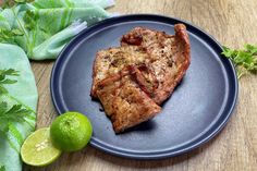 two pieces of meat on a blue plate next to limes