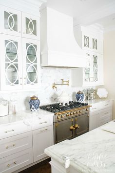 a white kitchen with marble counter tops and gold trim on the oven hood, cabinets, and drawers