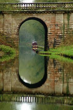 a small boat traveling under a bridge on a river next to grass and trees in the background