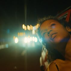 a man standing in the street at night with his head turned to the side and lights behind him